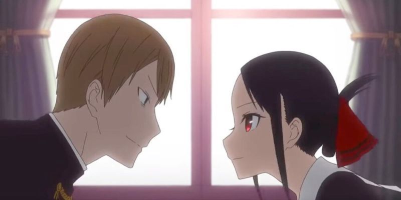 La imagen presenta una imagen de Kaguya-sama: Love is War: (De izquierda a derecha) Miyuki Shirogane (cabello corto y rubio y uniforme escolar negro) está mirando a Kaguya Shinomiya (cabello largo y negro con una cinta roja y uniforme escolar negro) .