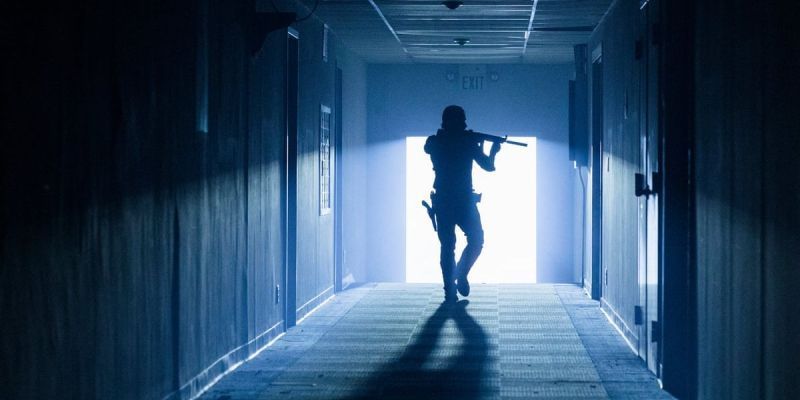 Eine Silhouette von Rick geht mit einem Gewehr in der Hand einen dunklen Flur entlang, ohne dass nur das Licht von der Tür nach draußen seinen Weg hinein beleuchtet